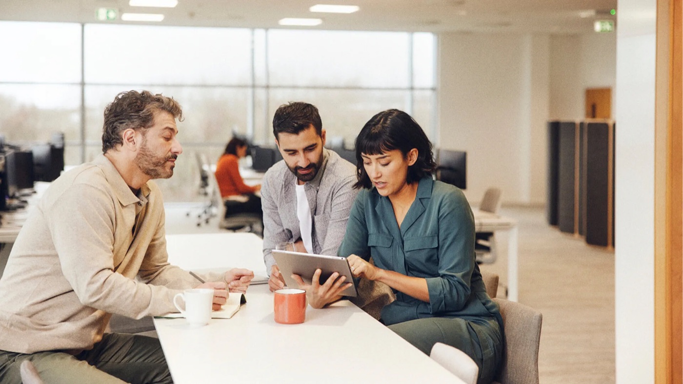Three colleagues reviewing data together on a tablet at a shared workspace
