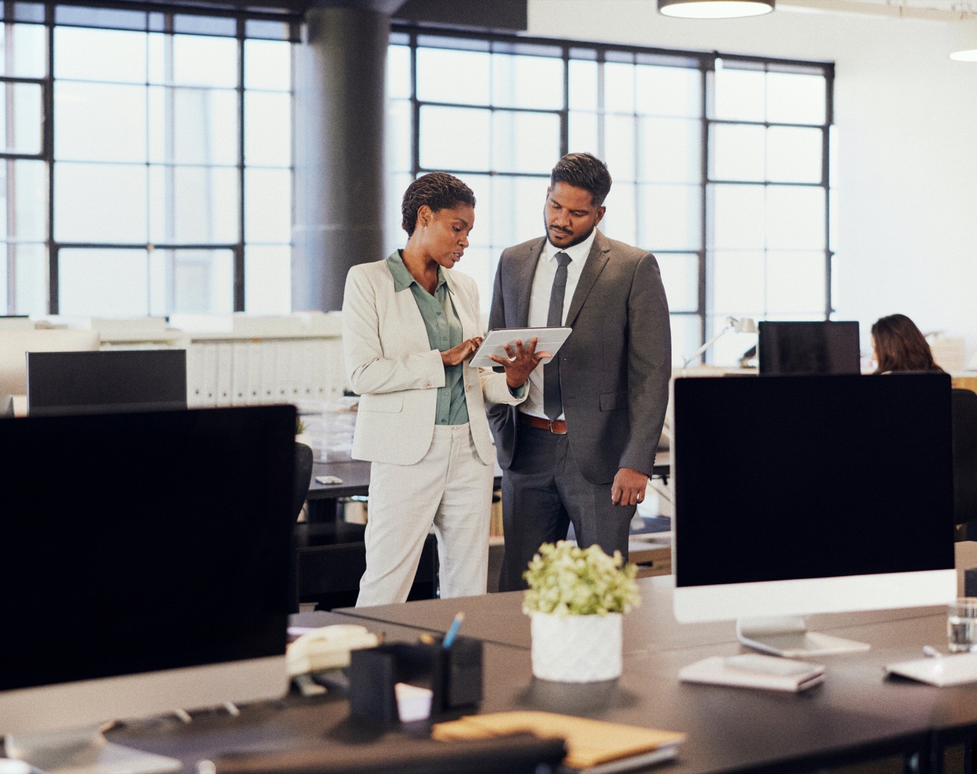 Two finance professionals reviewing figures on a tablet in an open-plan office